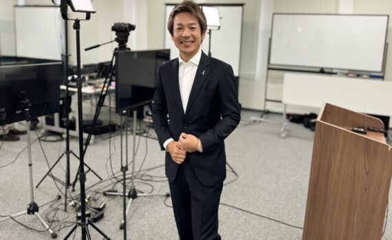 生命保険会社のウェビナー収録会場で撮影機材を背景に立つ清水健