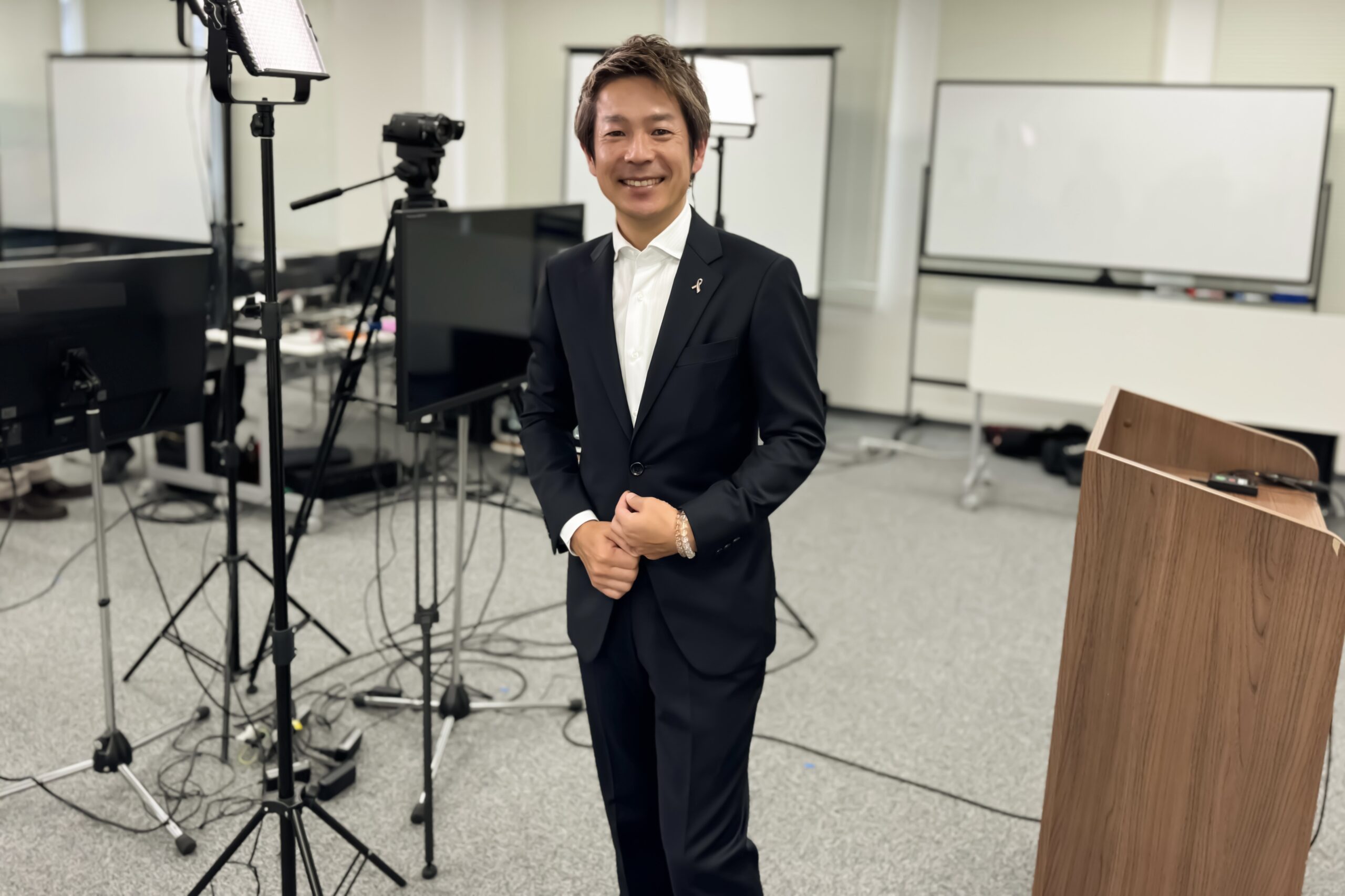 生命保険会社のウェビナー収録会場で撮影機材を背景に立つ清水健