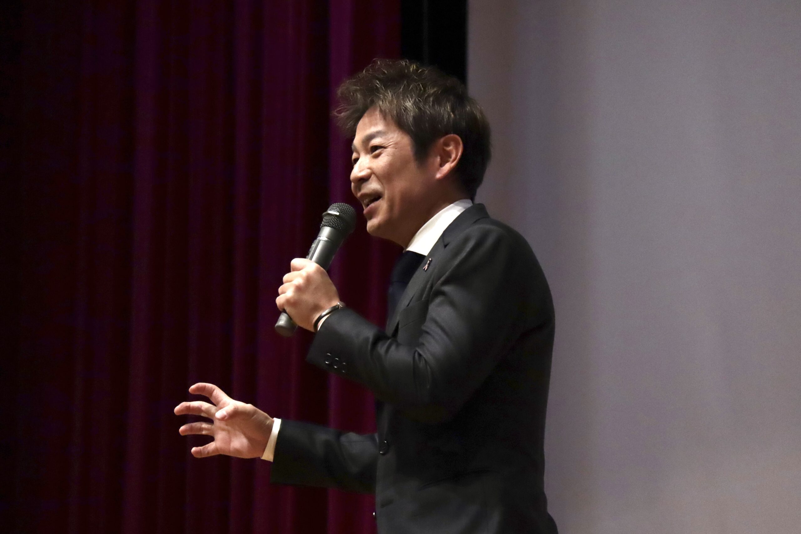講演会の壇上でマイクを手に話す清水健の姿