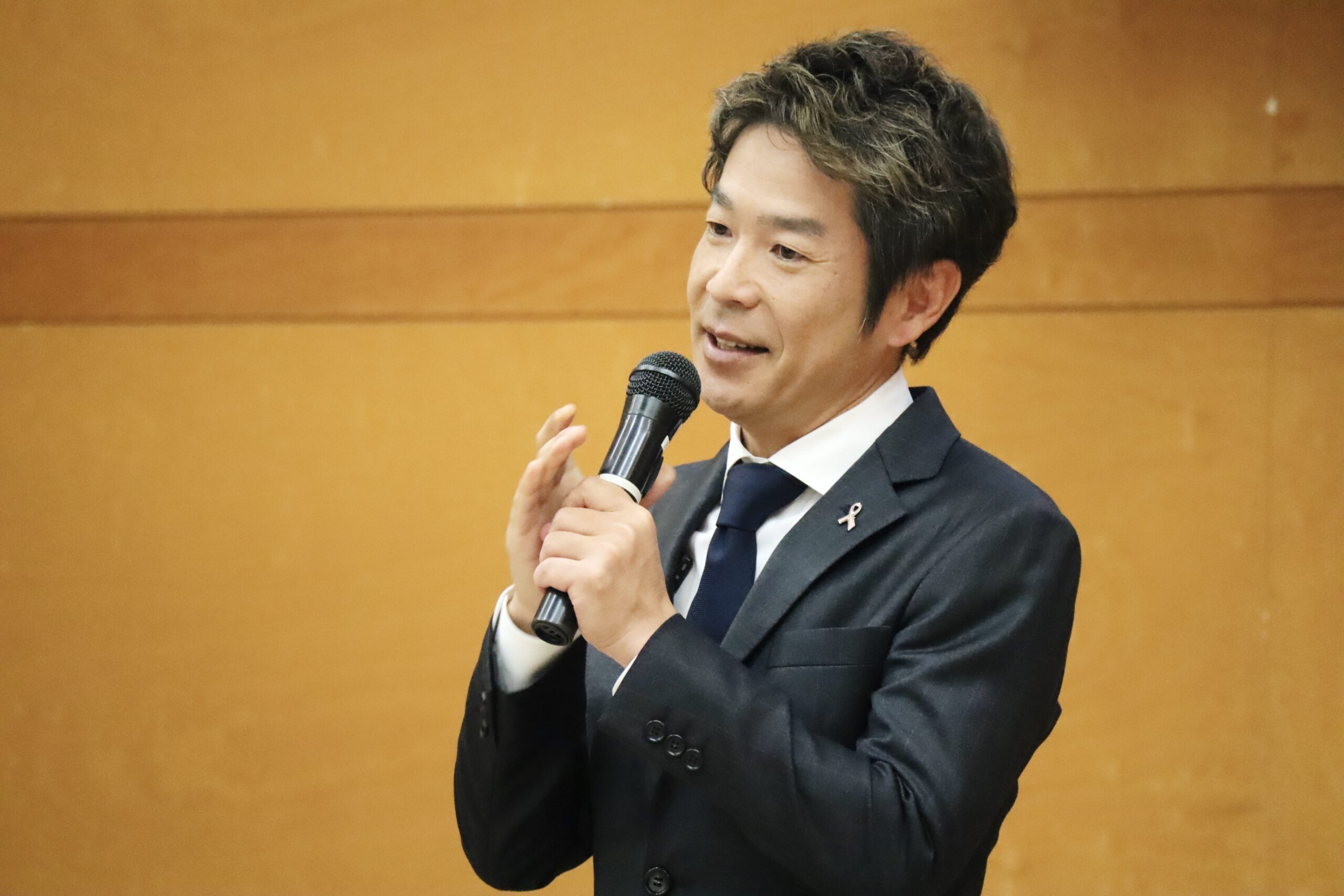 名張養護学園主催「子育て支援講演会」で、マイクを持ち講演する清水健。子どもたちと向き合うこと、支えることについて語る様子。